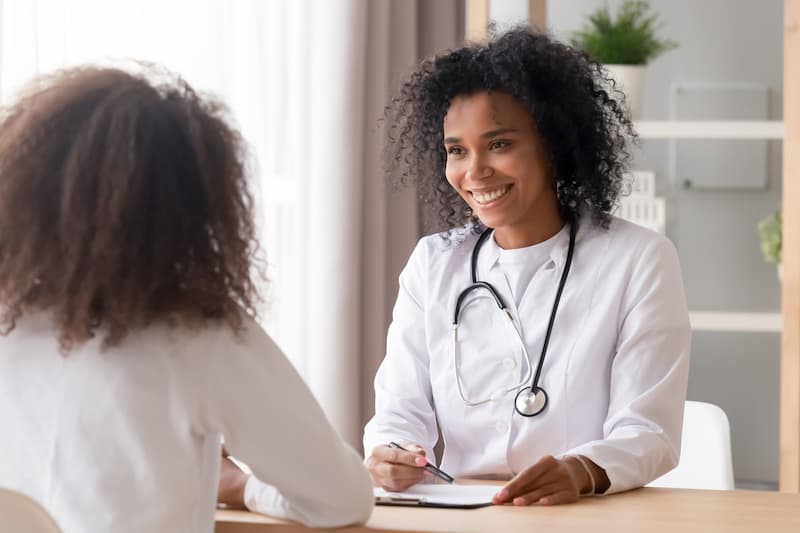 Smiling African female doctor talking to teen patient
